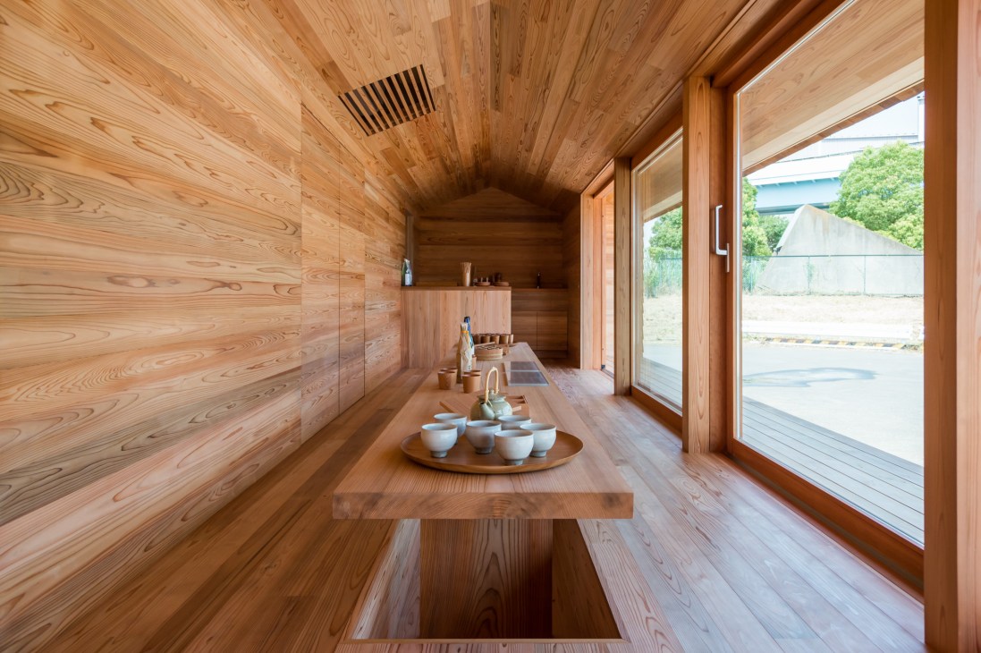 Interior of Yoshino-sugi Cedar House with wooden walls, floor and ceiling, a central wooden table with ceramic cups, and large windows overlooking exterior landscape.