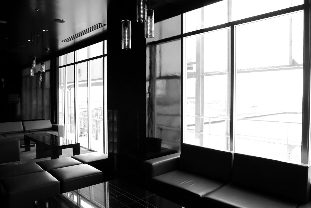 Modern cinema lounge with black seating, pendant lights, and floor-to-ceiling windows overlooking cityscape at United Cinemas.