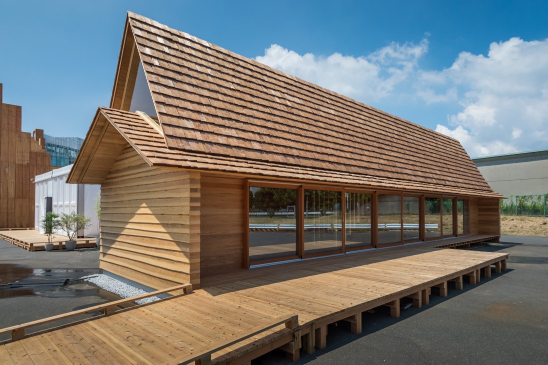 Modern wooden house with cedar siding, pitched roof, and large windows overlooking a terrace.