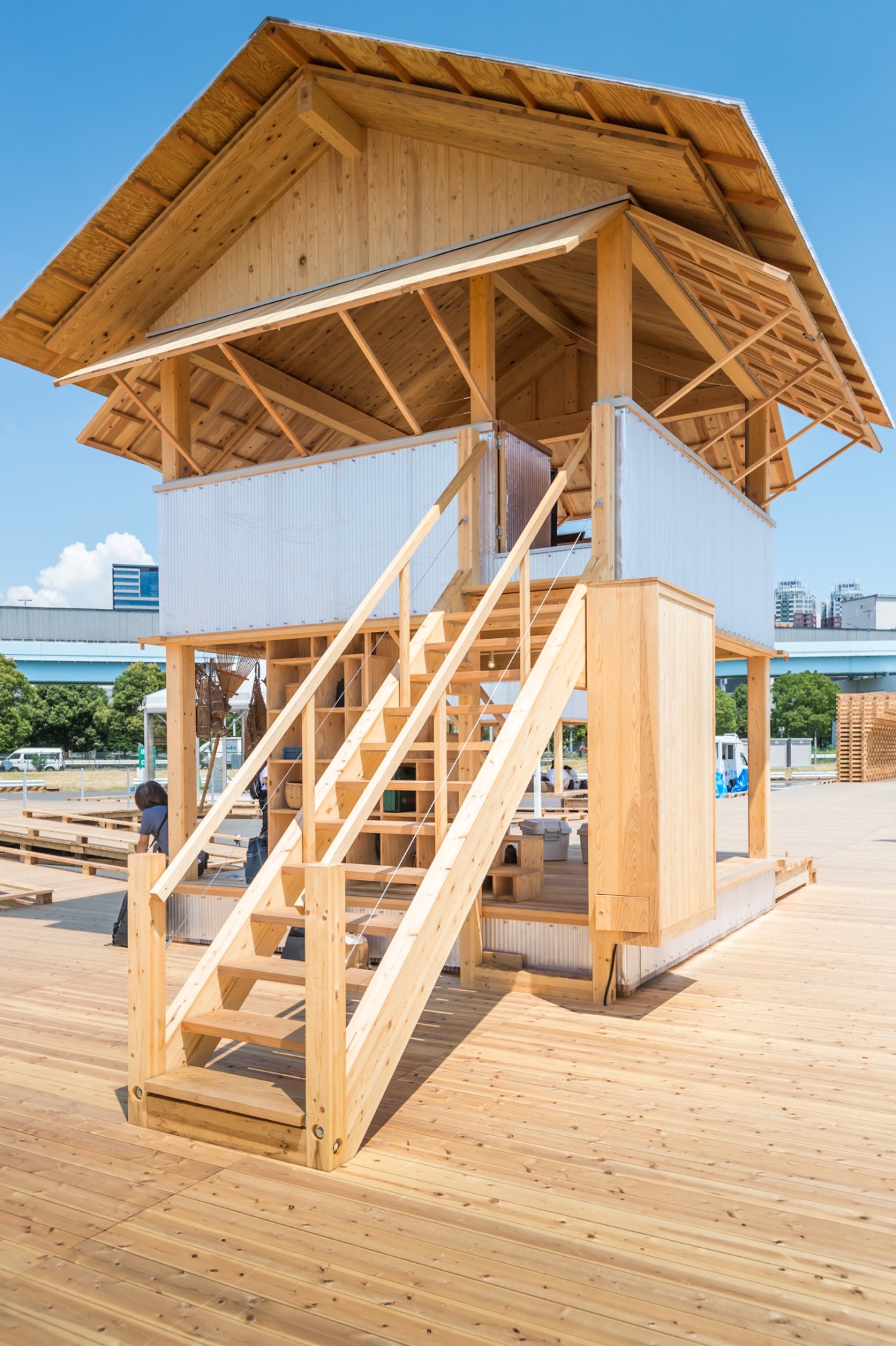 Wooden tower structure with large overhanging roof and open staircase at House Vision exhibition.
