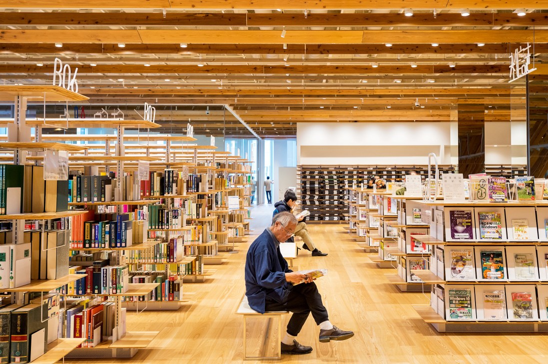 An elderly man reads in Toyama City Public Library's bright wooden interior, designed by Kengo Kuma.