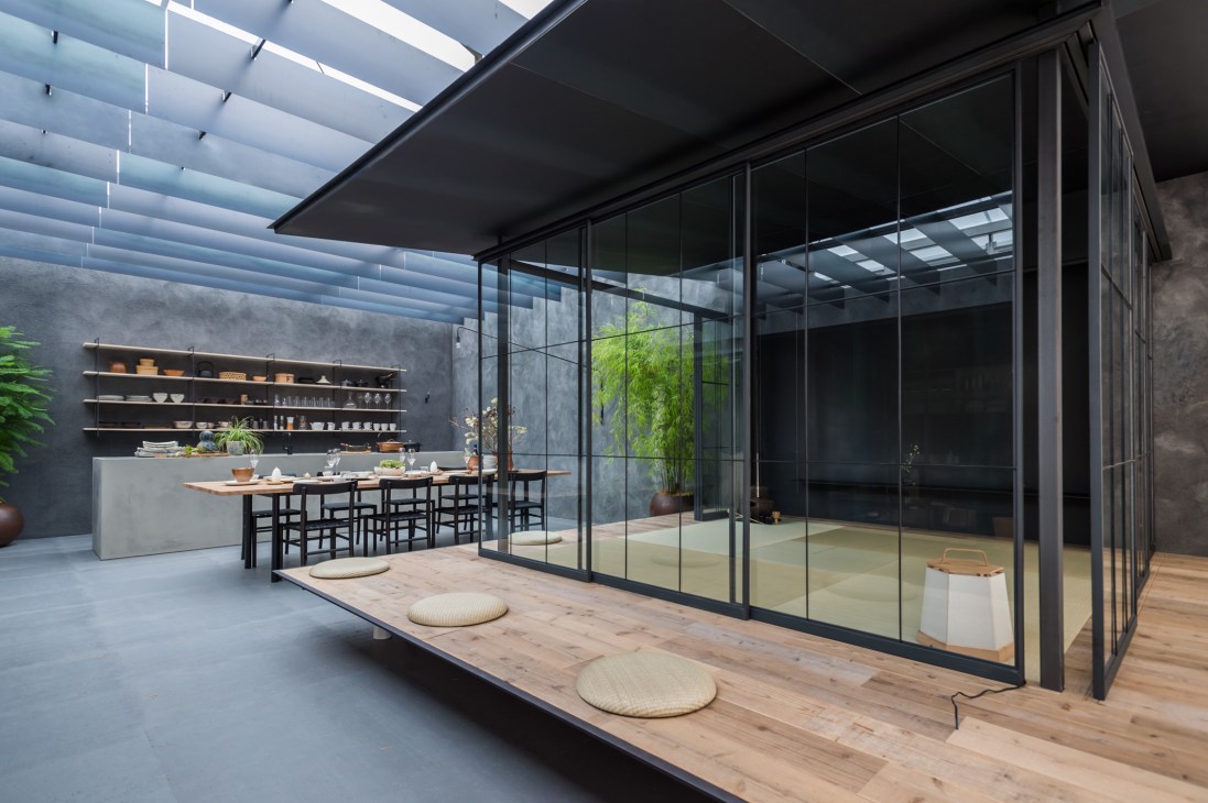 Modern minimalist kitchen and dining space with black-framed glass walls, wooden countertop, and shelving.