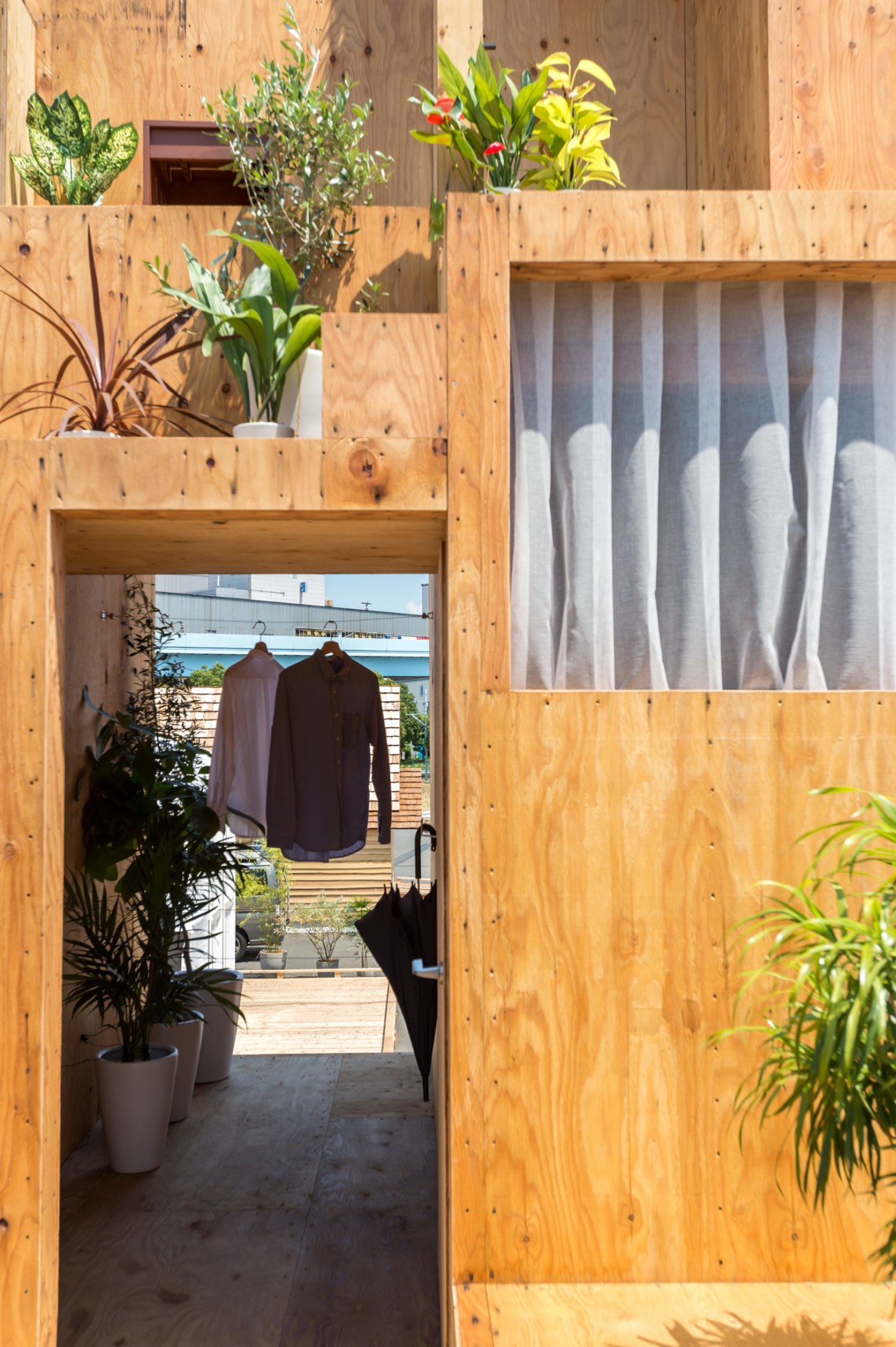 Wooden stacked shelving unit with potted plants and clothing visible through an open passage.