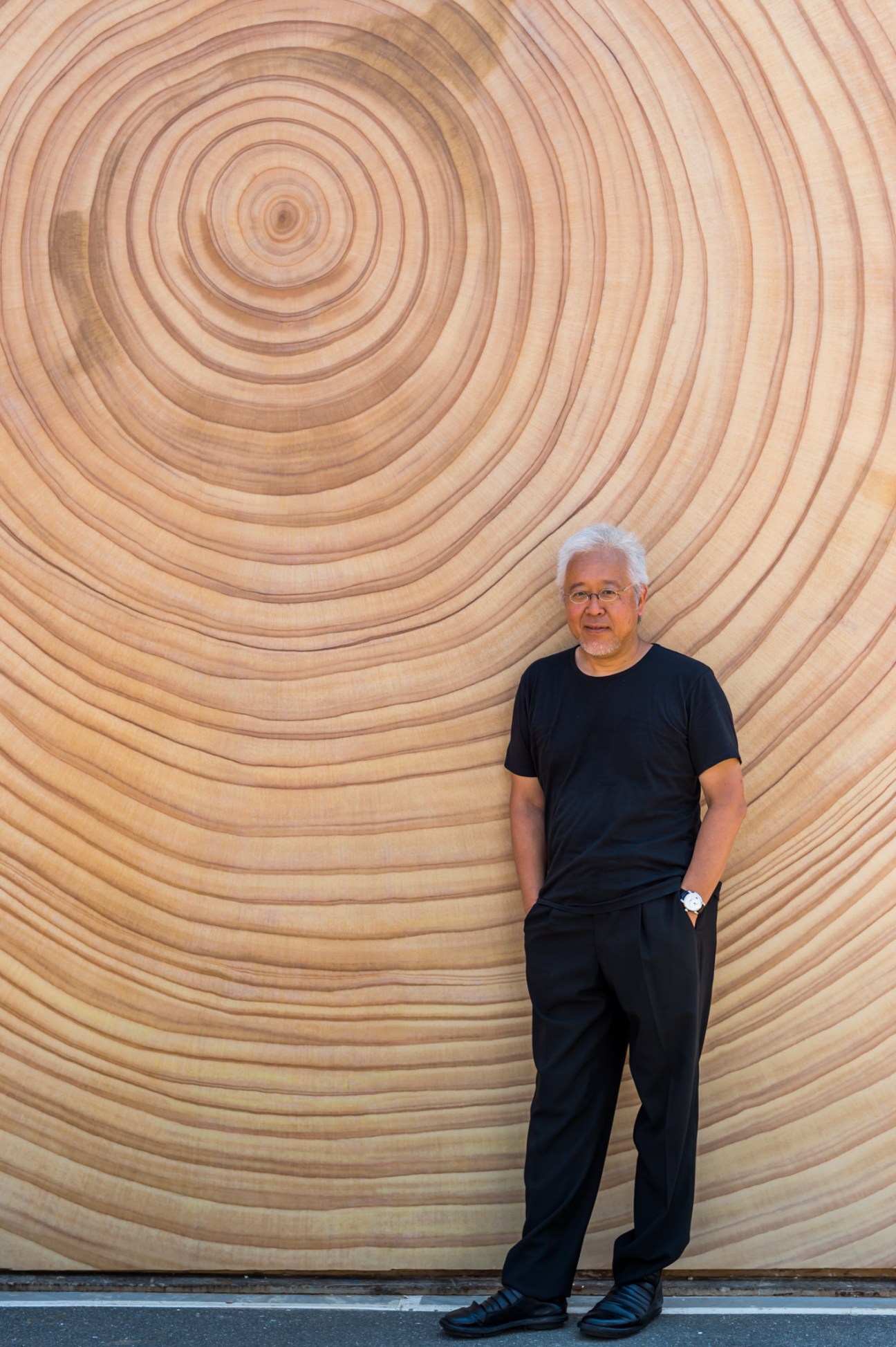 Kenya Hara stands against a wooden wall with concentric circular rings at the House Vision exhibition