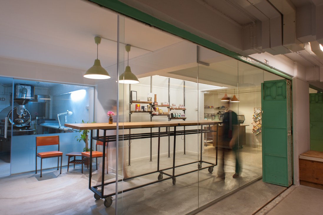 Interior of Nylon Coffee roastery in Singapore with glass partitions, wooden counter, pendant lights and modern minimalist design.