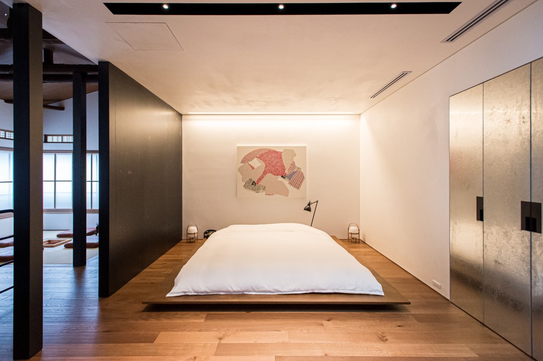 Minimalist bedroom with low platform bed, white bedding, and abstract red artwork on wall at Trunk House Tokyo.