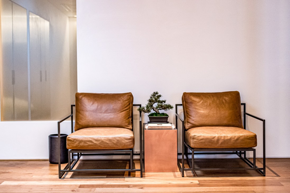 Two tan leather Stephen Kenn armchairs with black metal frames facing each other across a small side table with a bonsai plant and books.