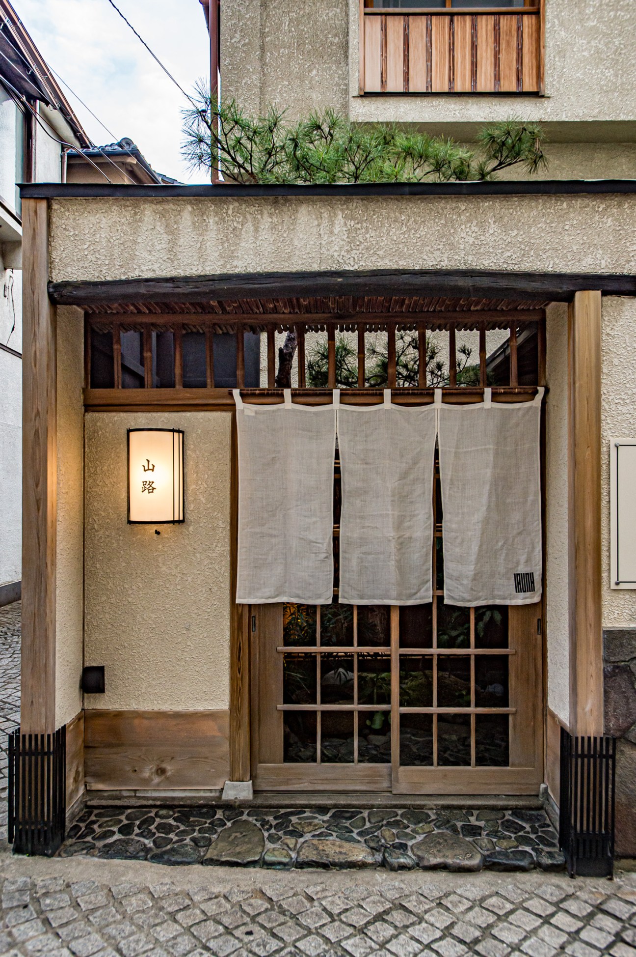 Traditional Japanese wooden entrance to Trunk House holiday home with white noren curtains and illuminated sign.