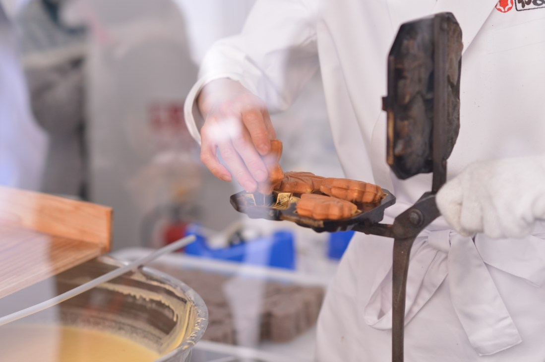 A confectioner's hand places maple-leaf shaped momiji manju cakes into a traditional mold.