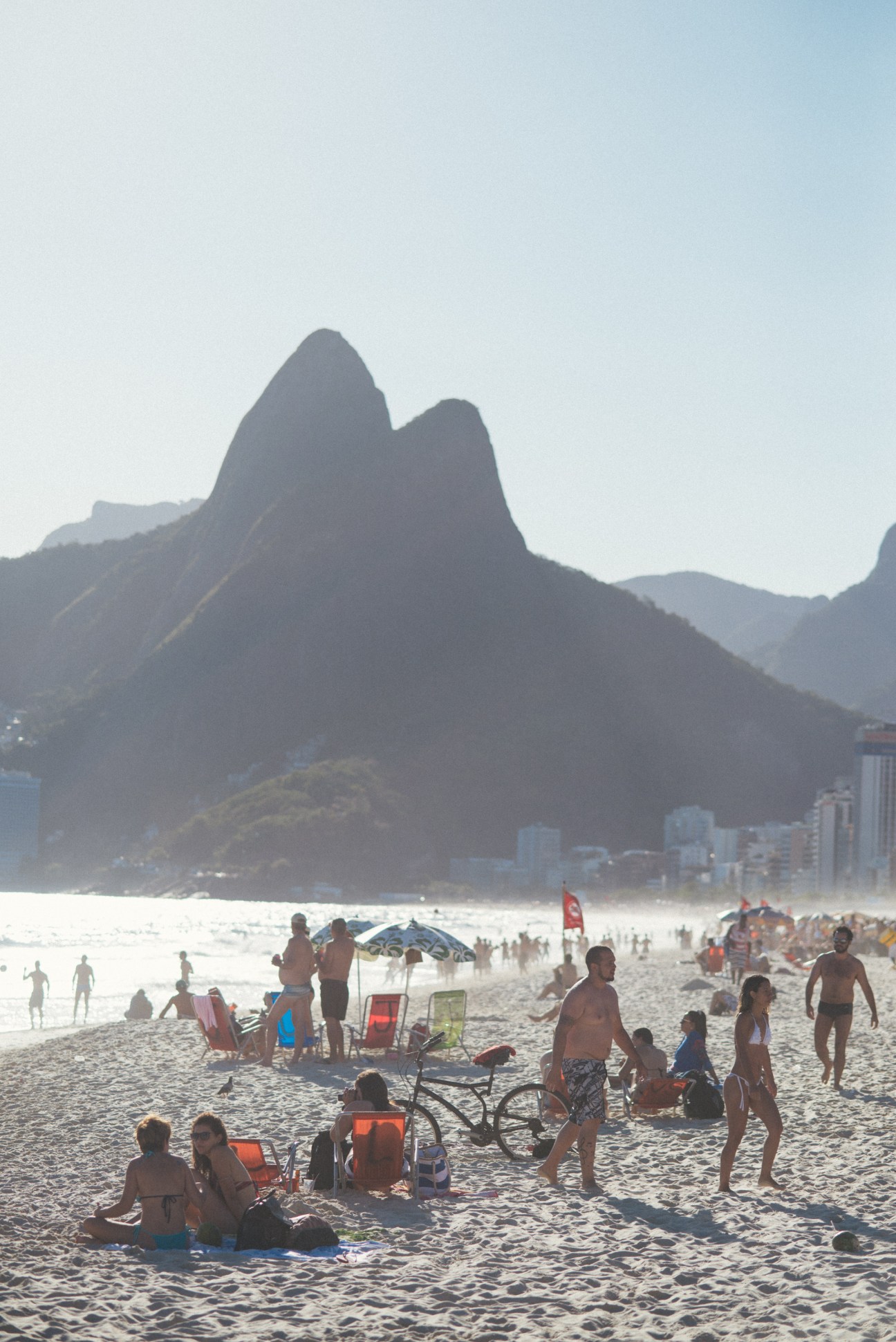 Crowded Ipanema Beach with distinctive mountains in the background and beachgoers relaxing on sand.