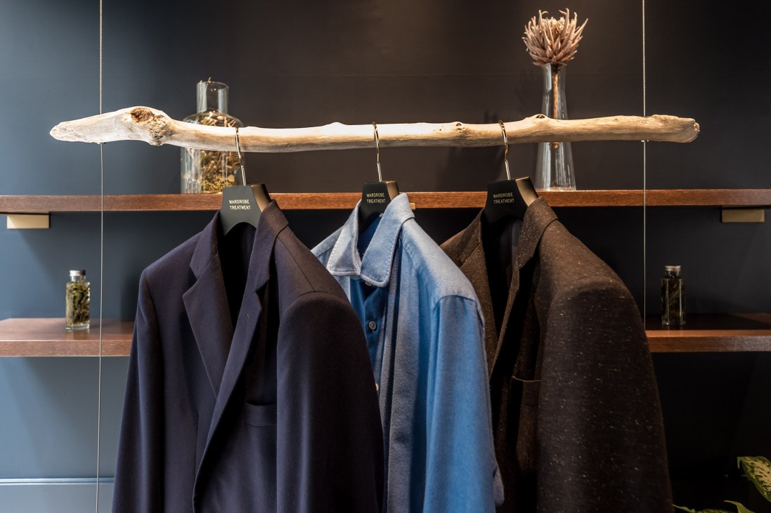 Cleaned garments hanging on a wooden rail with Wardrobe Treatment labels in a minimalist shop interior.