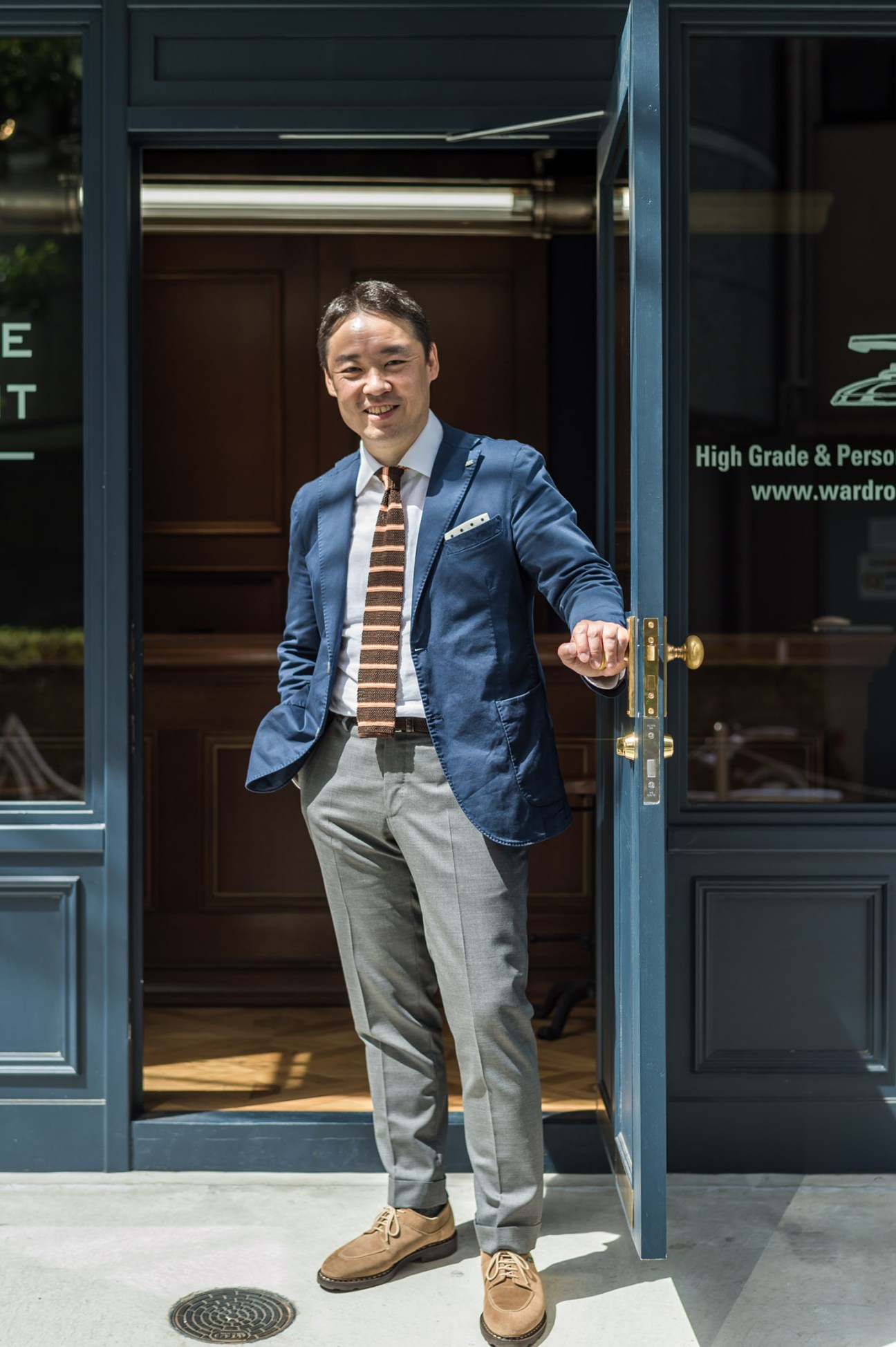 Yoichiro Teramae stands smiling in the doorway of his Tokyo drycleaning shop, Wardrobe Treatment.