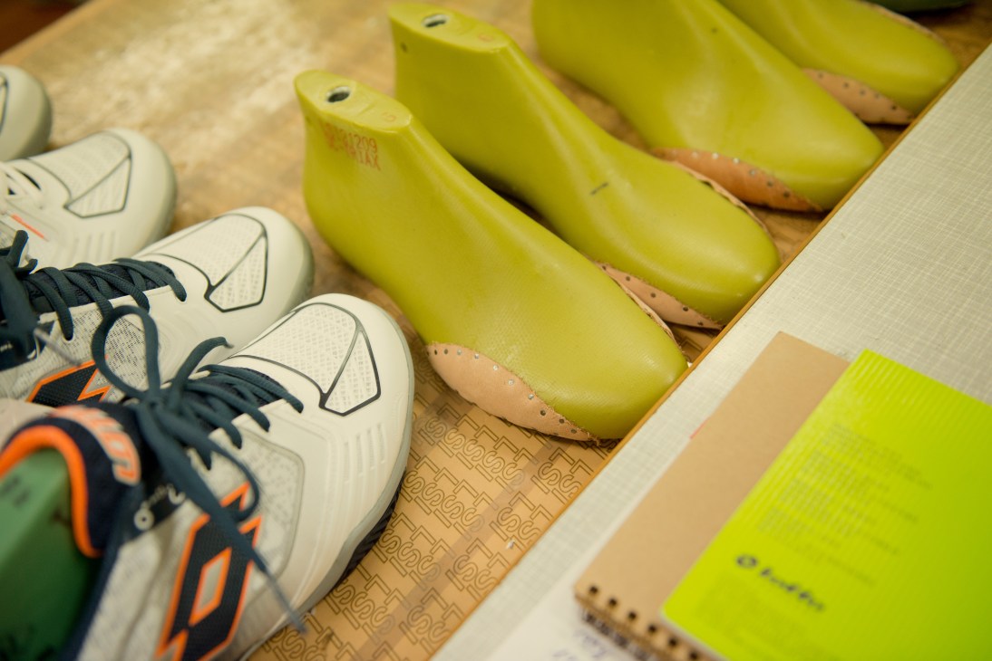 White sneakers with black laces and orange accents next to lime-green shoe lasts on a wooden surface