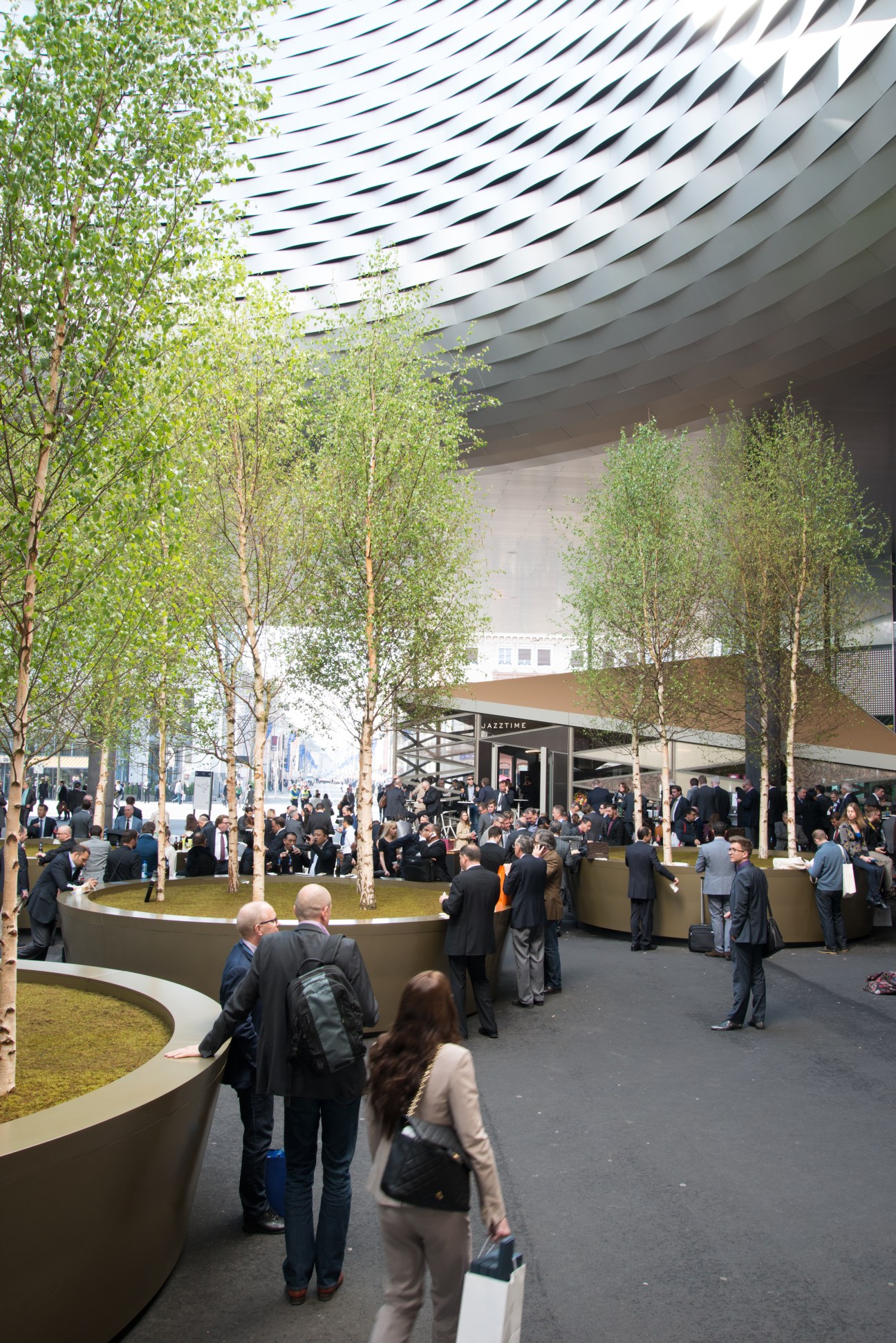 Interior of Baselworld's Herzog & de Meuron-designed Hall 1 with attendees, trees, and striking geometric ceiling.