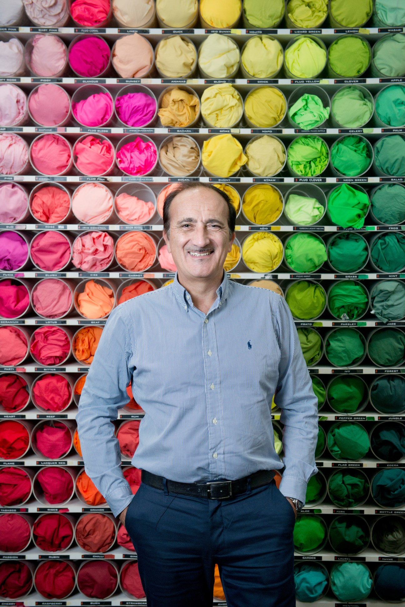 Lotto's president Andrea Tomat stands smiling in front of a wall of colorful shoe material swatches.