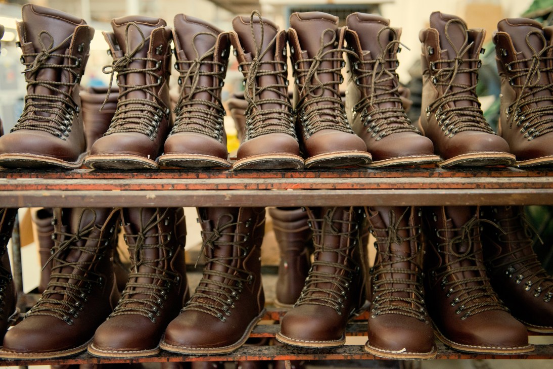 Brown leather hiking boots with laces displayed on two wooden shelves.