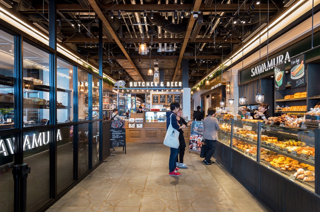 Interior of Newoman retail complex at Shinjuku Station showing bakery and food shops with customers