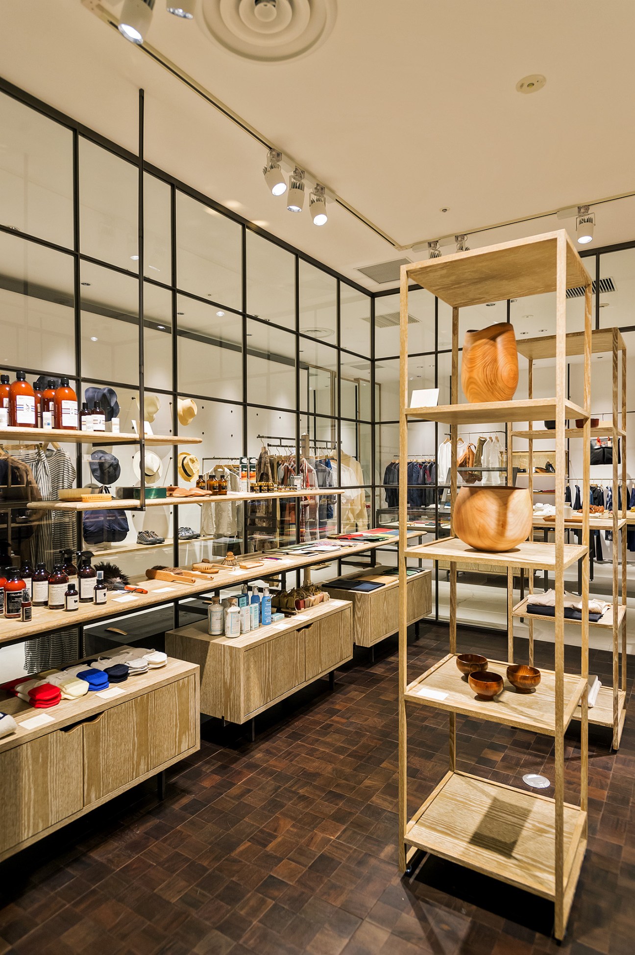 Interior of a modern retail shop with wooden shelving, glass partitions, and displayed merchandise including clothing and accessories.