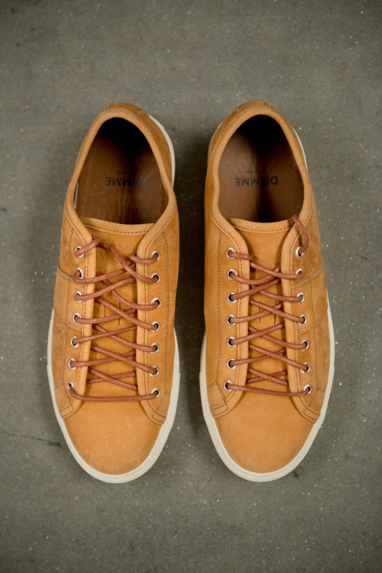 Pair of tan leather lace-up boots with white soles and burgundy laces, displayed from above on concrete.