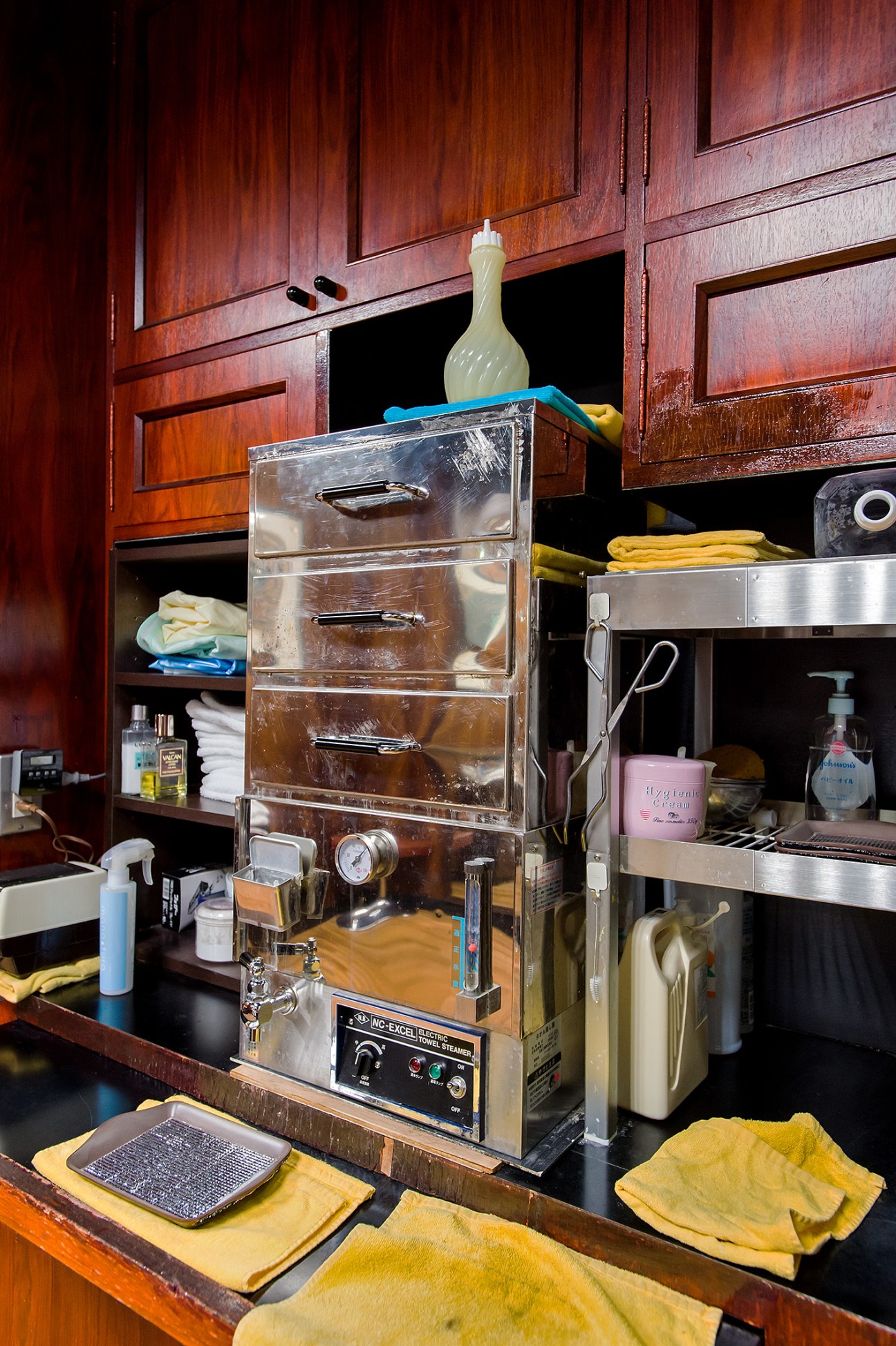 Barber steaming station with wooden cabinets, metal drawers, and grooming supplies at Barber Oikawa in Tokyo.
