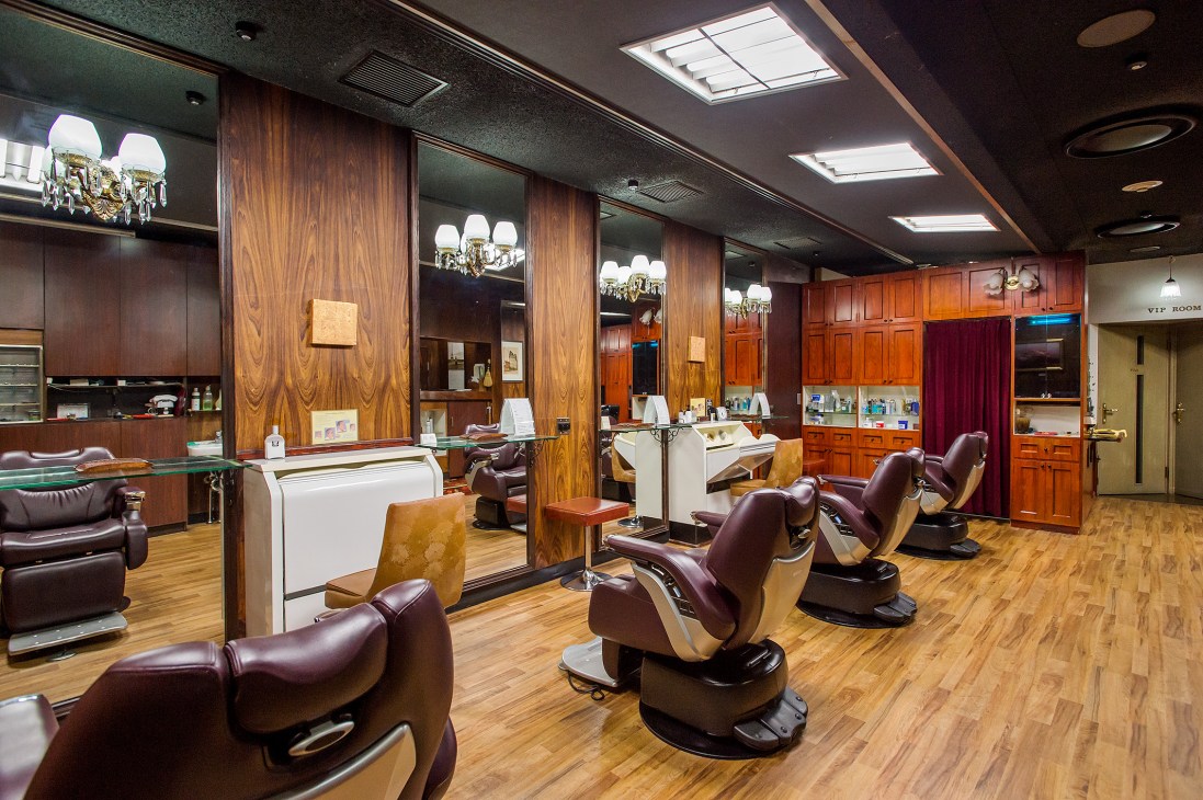 Interior of Barber Oikawa Tokyo with vintage barber chairs, wooden paneling and chandeliers.
