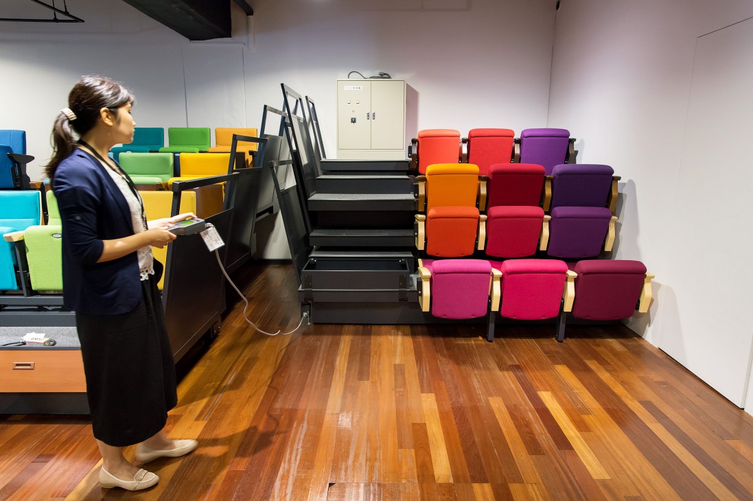 Woman viewing colorful retractable theatre seats displayed in Kotobuki Seating's showroom.