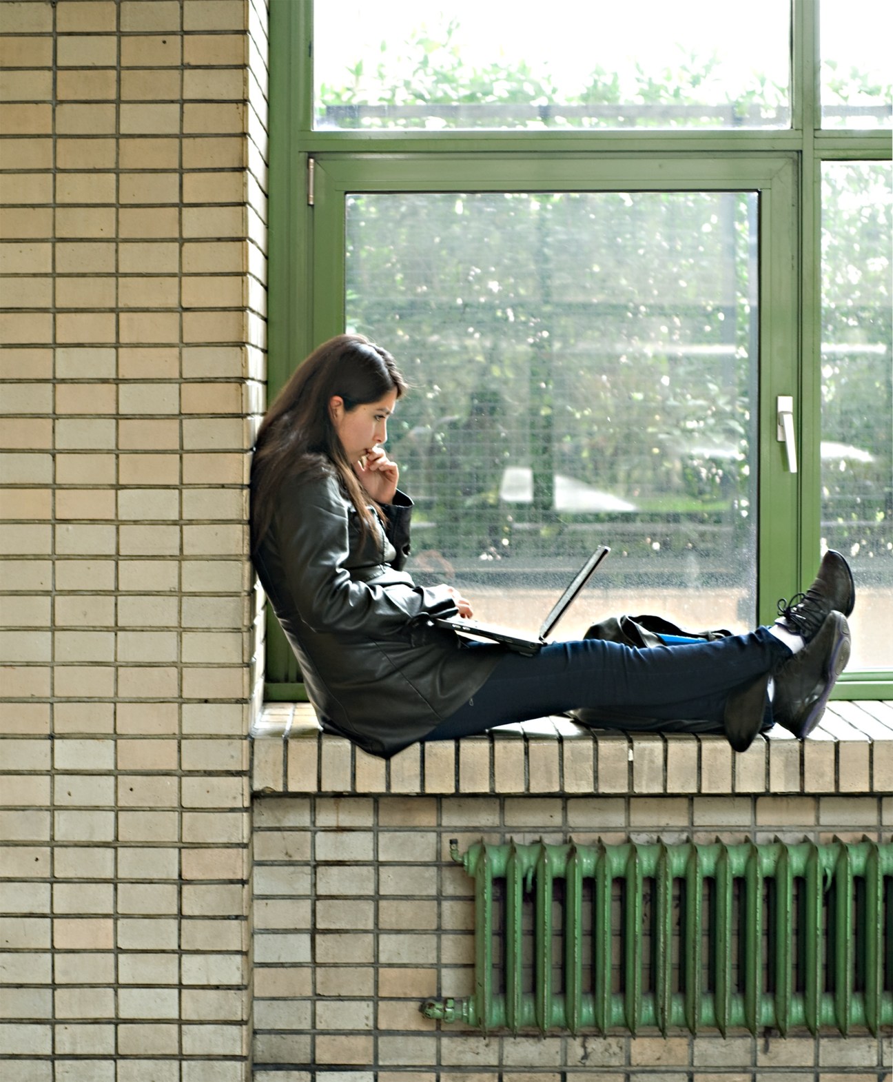 MBA student sitting on a windowsill working on a laptop at SDA Bocconi.