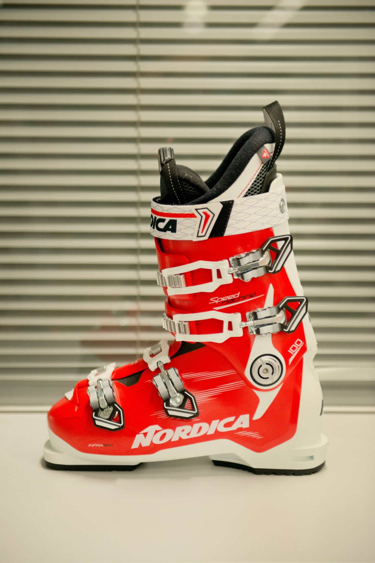 Red and white Nordica ski boot with metal buckles against a corrugated metal background.