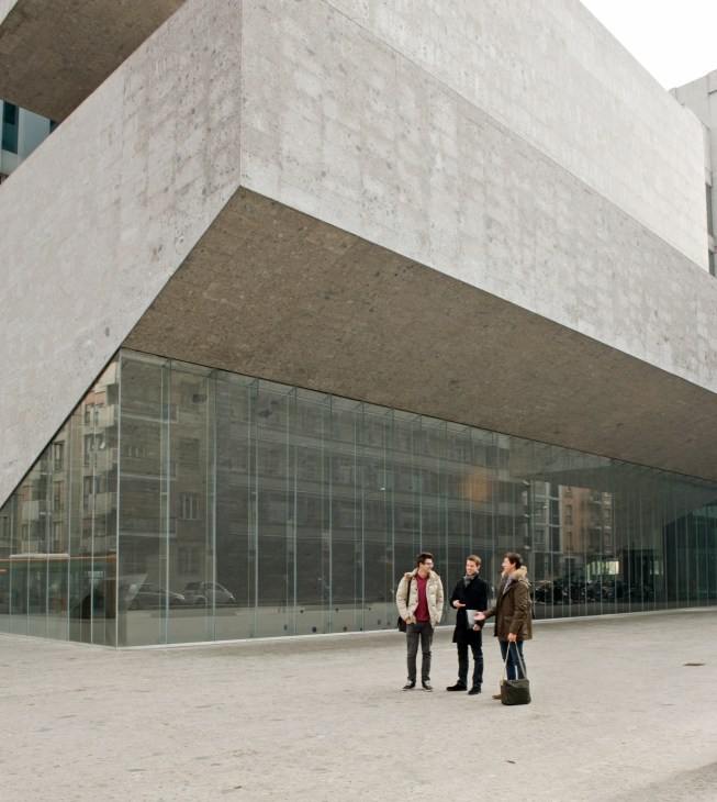 Three people standing in front of SDA Bocconi's award-winning glass and stone faculty building designed by Grafton Architects.