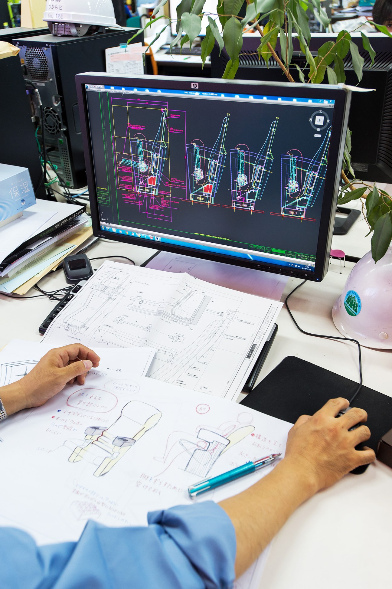 Engineer reviews technical blueprints and CAD designs at workstation in design laboratory.