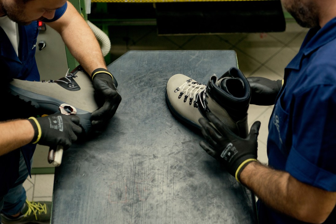 Workers in blue uniforms and black gloves inspect hiking boots on a work table at Scarpa factory.