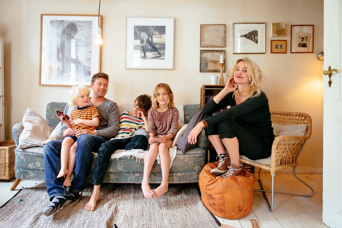 Marie Storaas, husband Snorre Saveraas and their family sitting together in a small living room decorated with framed artwork.