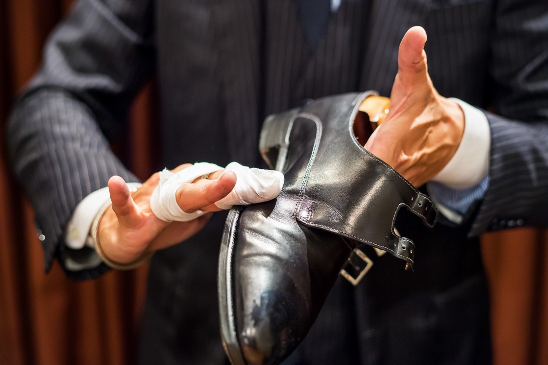 Hands with white gloves polishing a black leather shoe at Brift H shoe-care salon in Tokyo.