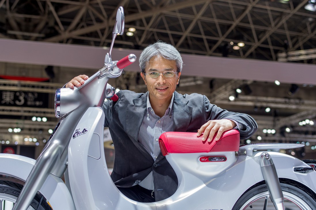 Tokumaru Watanabe, Honda designer, poses with the white EV-Cub electric scooter at Tokyo Motor Show.
