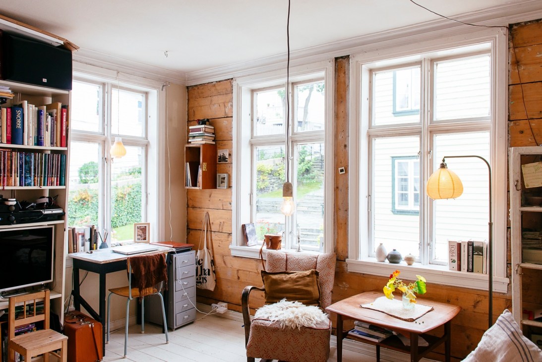 Bright interior of a renovated wooden home showing workspace, seating area, bookshelves and large windows overlooking Bergen.