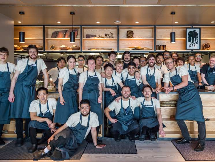 Inua restaurant kitchen team of chefs in blue aprons posing together, led by head chef Thomas Frebel in front right.