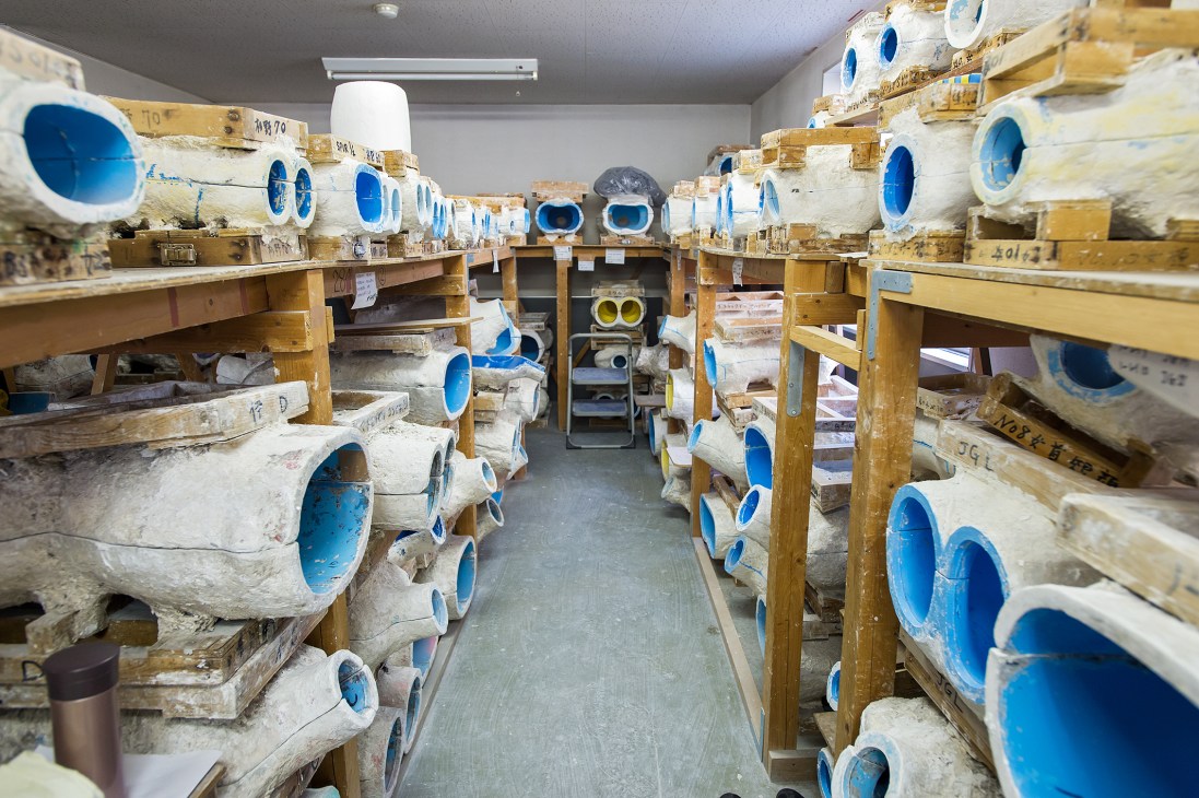Wooden shelves filled with white plaster mannequin moulds with blue interior sections in Kiiya's workshop.