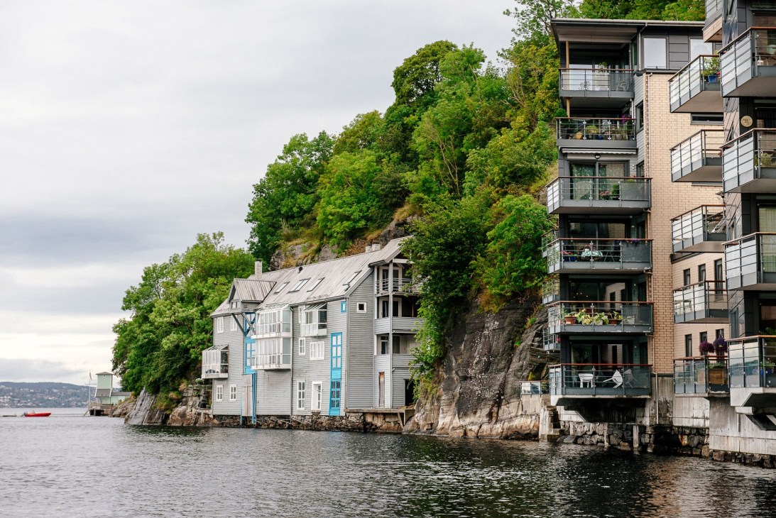 Waterfront apartment complex with modern balconies next to traditional white wooden houses on rocky shore in Bergen.