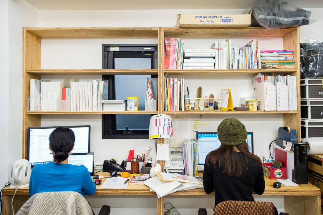 Two people work at a wooden desk with integrated shelving in Kota Engaku's editorial office at Ridge Shoto.