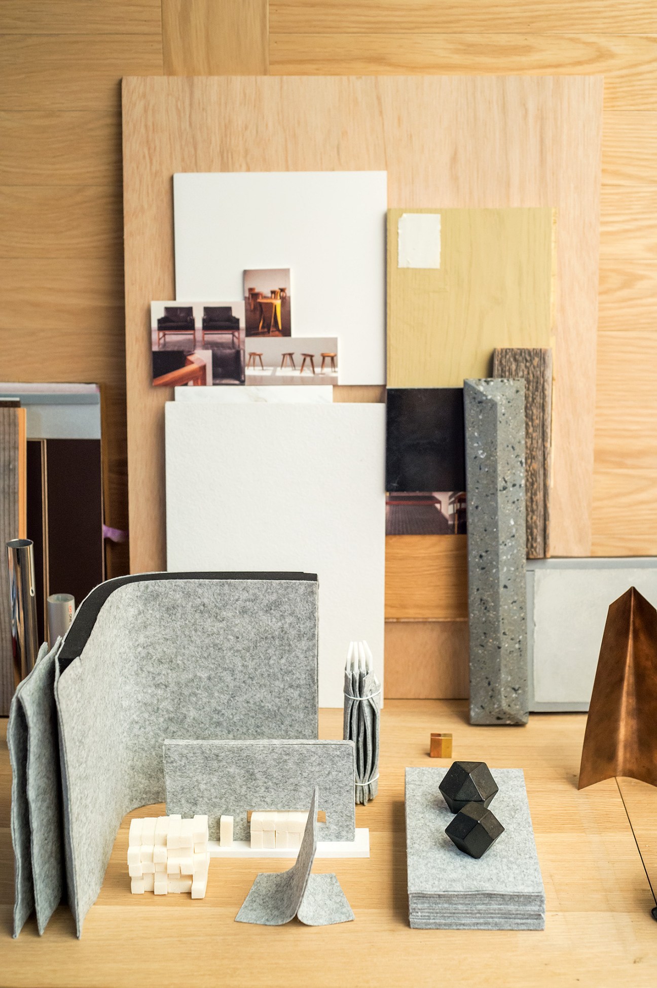 Material samples and design objects arranged on a wooden surface, including felt, concrete, wood, and metal pieces.