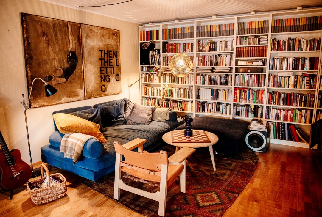 Living room with blue sofa, floor-to-ceiling white bookshelves, wooden furniture, and artwork on walls.