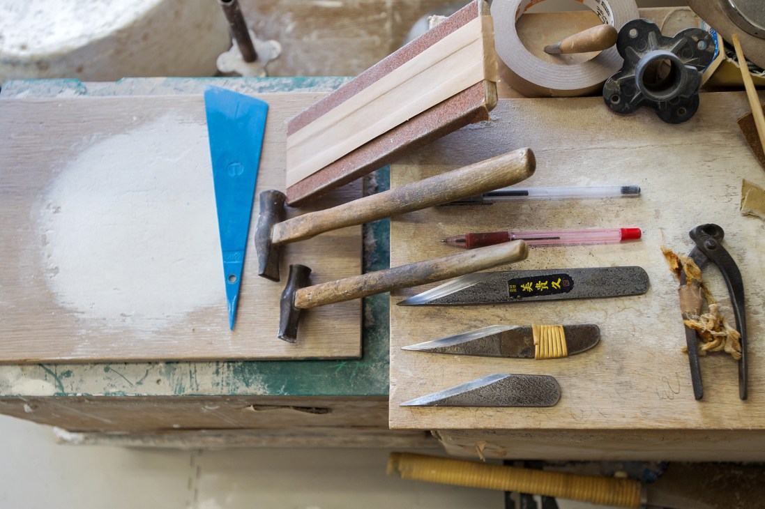 Crafting tools including hammers, chisels, knives and scrapers arranged on a wooden workbench at Kiiya's atelier.