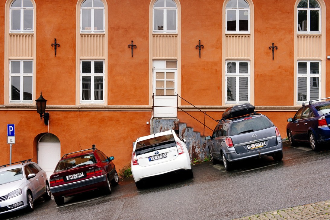 Orange residential building with parked cars and a handicap parking sign in Bergen's Nordnes neighbourhood.