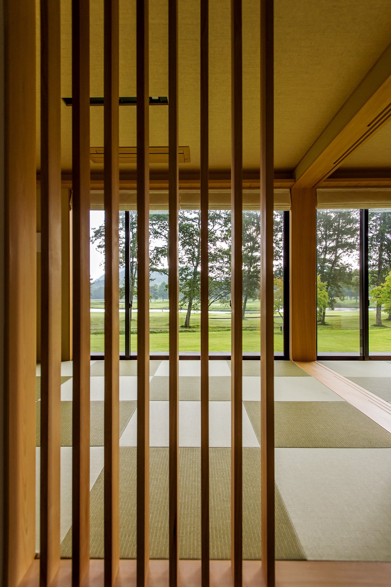 Wooden slat partition with view of green lawn and trees beyond through large windows in a Japanese retreat.