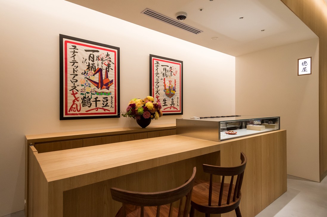 A traditional Japanese confectionery counter with wooden seating, display cases, and framed artwork on the wall
