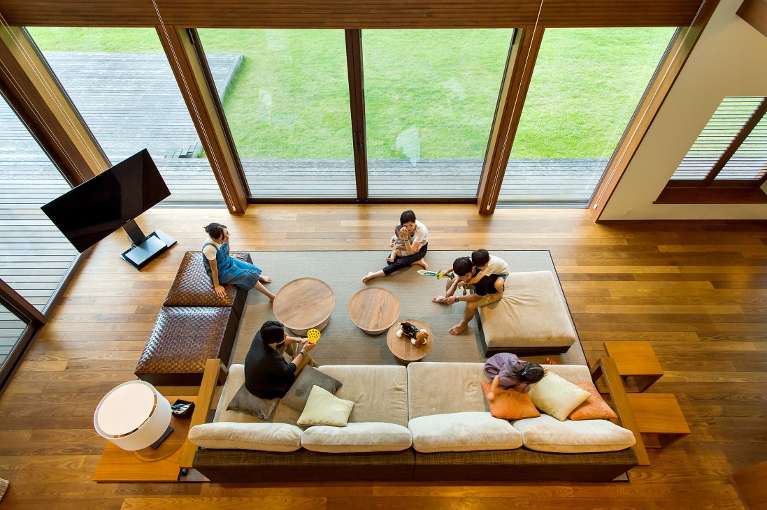 Overhead view of Beams By The Green living room with employees and families relaxing on sofas and floor mats with large glass doors overlooking lawn.