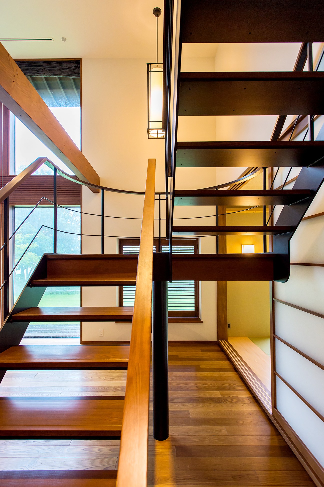 Wooden staircase with dark railings leading upstairs in a modern Japanese retreat house.