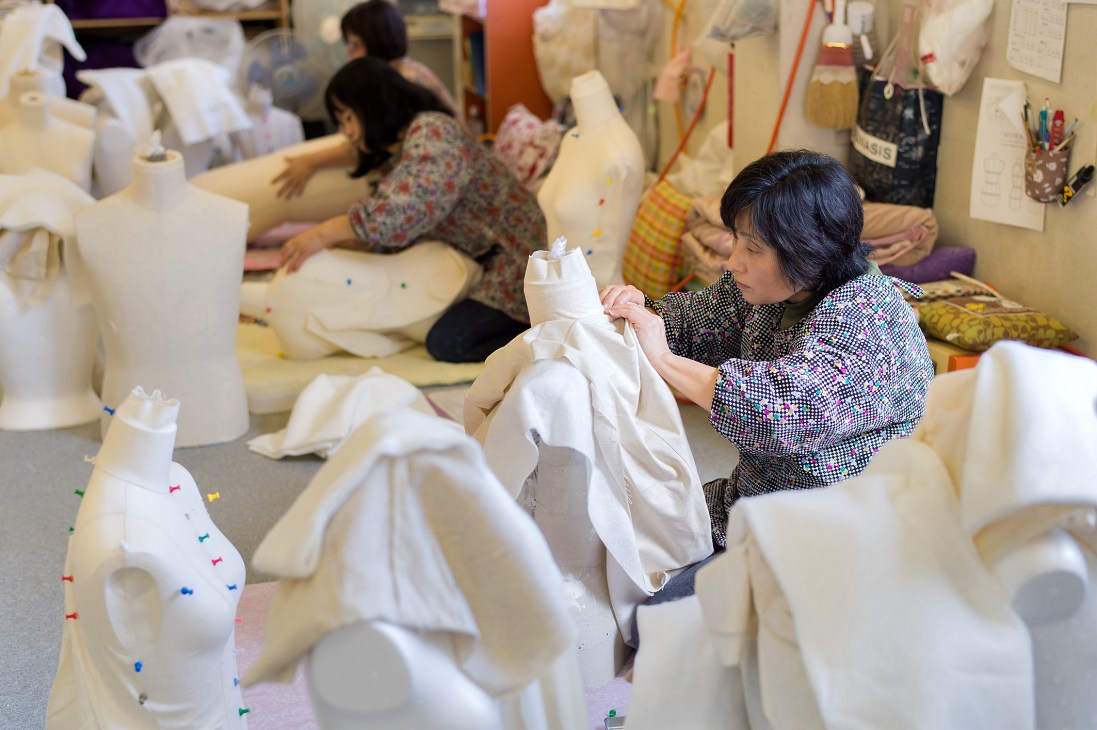 Kiiya factory employee stitching white cloth onto a mannequin torso among many other dress forms.