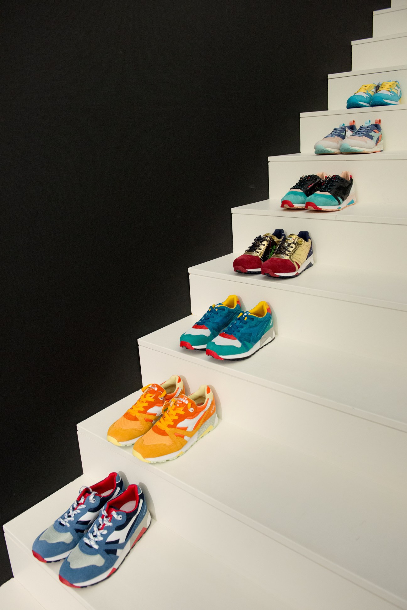 Colorful Diadora sneakers displayed on white steps against a dark background.