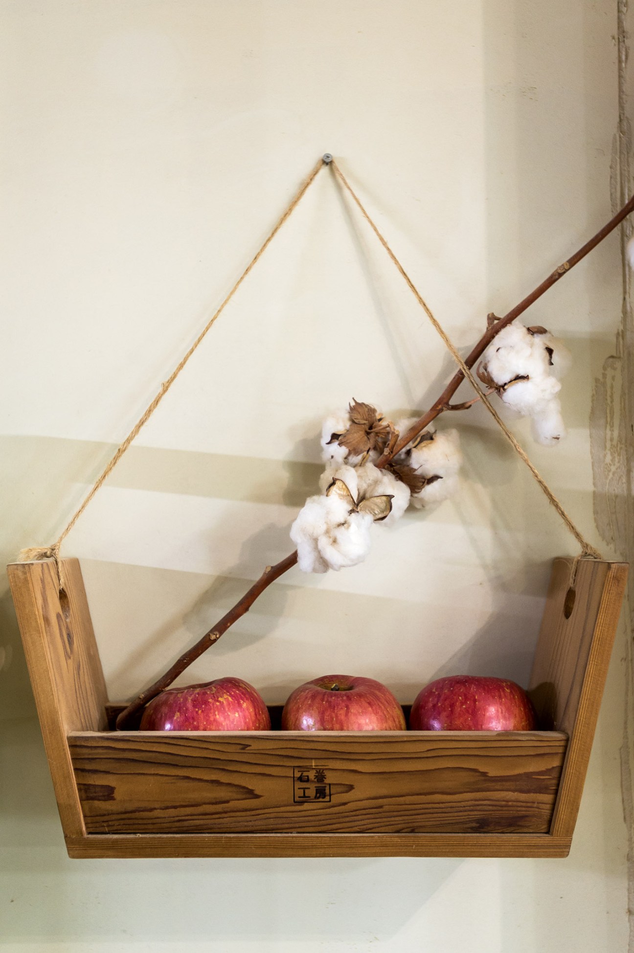 Wooden carry stool with rope handles displaying red apples and cotton flowers, branded with Japanese characters.